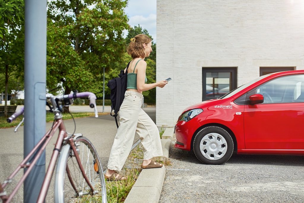 Bild 2. Schritt: Anmelden - Person mit Handy läuft zum stadtmobil-Auto